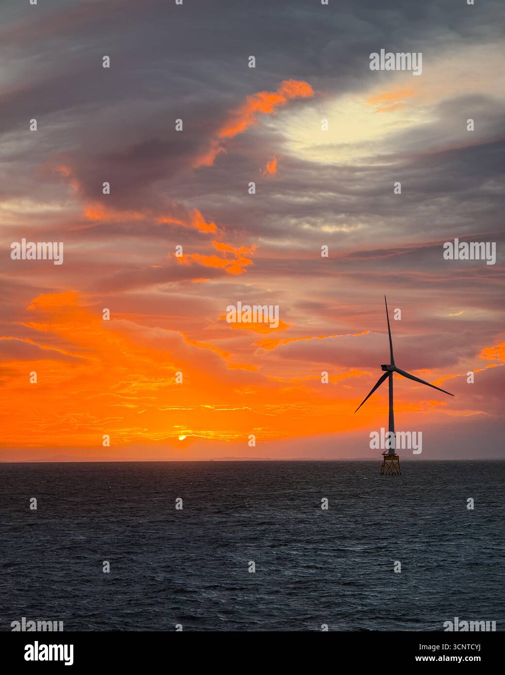 Éolienne offshore au coucher du soleil sur la mer du Nord, ciel orange spectaculaire et eaux sombres de l'océan, scène d'énergie renouvelable. Banque D'Images Éolienne offshore au coucher du soleil sur la mer du Nord, ciel orange spectaculaire et eaux sombres de l'océan, scène d'énergie renouvelable. Banque D'Images