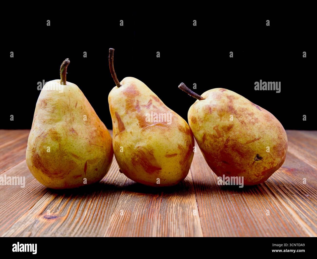 Trois vieilles poires mûries se tiennent sur une planche de bois dans un cadre de nature morte. Banque D'Images