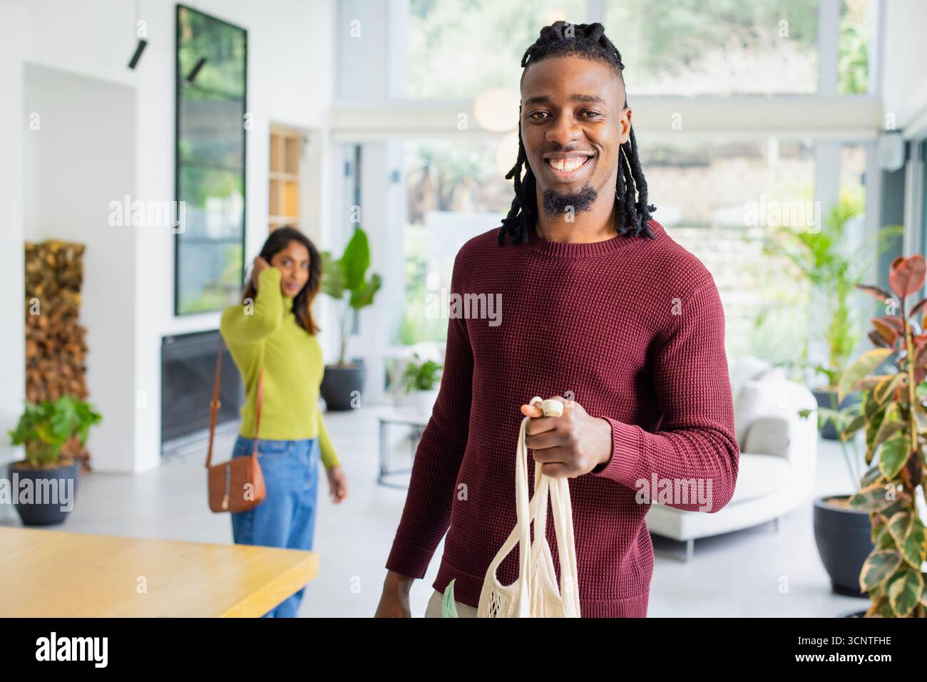 Couple diversifié parlant au téléphone et portant sac fourre-tout en toile dans le salon avec bois de chauffage Banque D'Images
