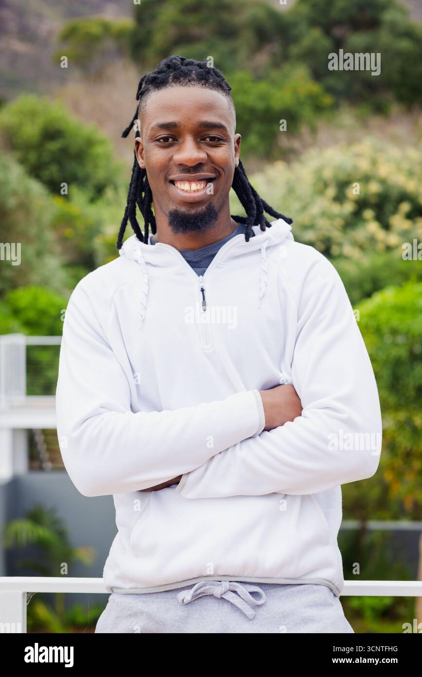 Homme afro-américain debout avec les bras croisés sur la terrasse par une balustrade en métal portant un sweat à capuche blanc Banque D'Images