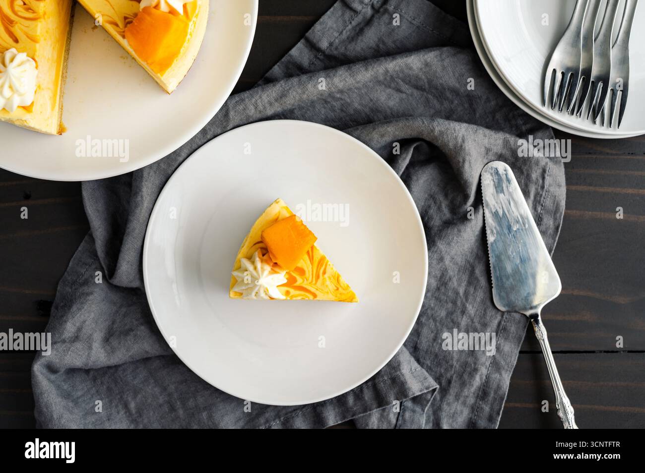 Tranche de gâteau de mousse de mangue sur une assiette vue de dessus : morceau de gâteau de mousse tourbillonnée avec serveur à gâteau, fourchettes et support à gâteau en arrière-plan Banque D'Images