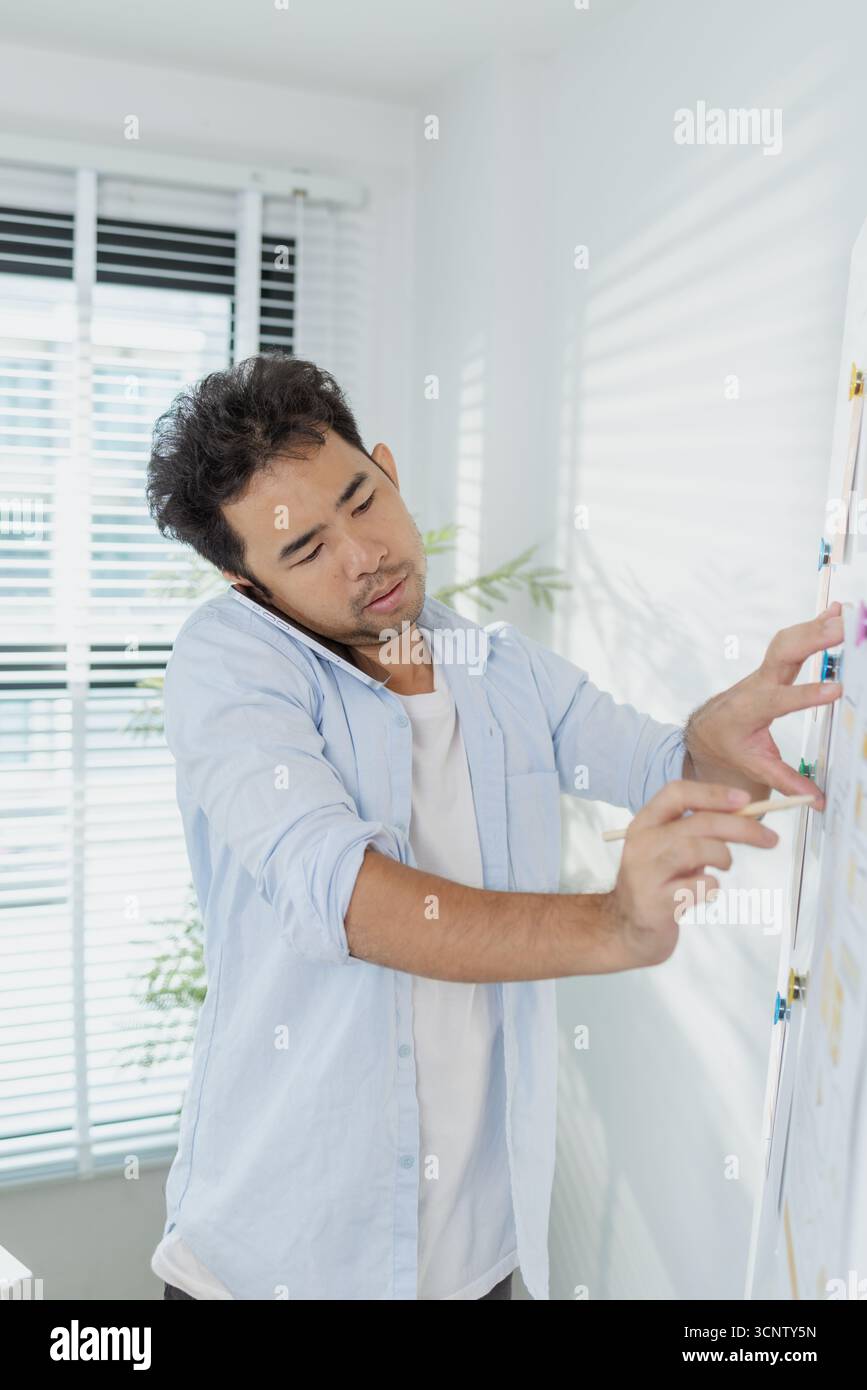 Un concepteur créatif travaille sur la planification UX/UI, analysant des croquis et des prototypes sur un tableau blanc tout en utilisant un ordinateur portable. Le processus montre la pensée de conception Banque D'Images