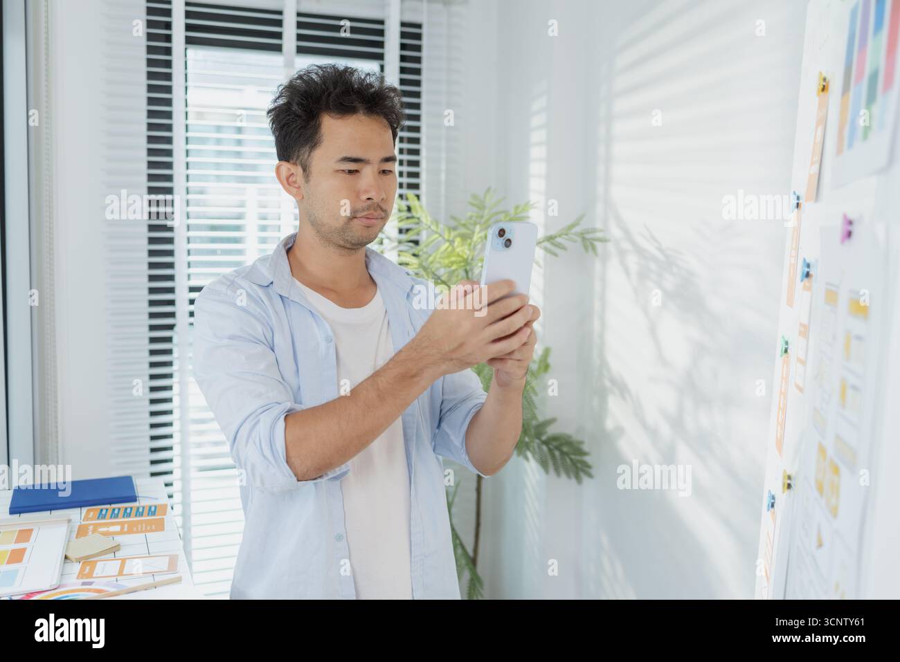 Un concepteur créatif travaille sur la planification UX/UI, analysant des croquis et des prototypes sur un tableau blanc tout en utilisant un ordinateur portable. Le processus montre la pensée de conception Banque D'Images