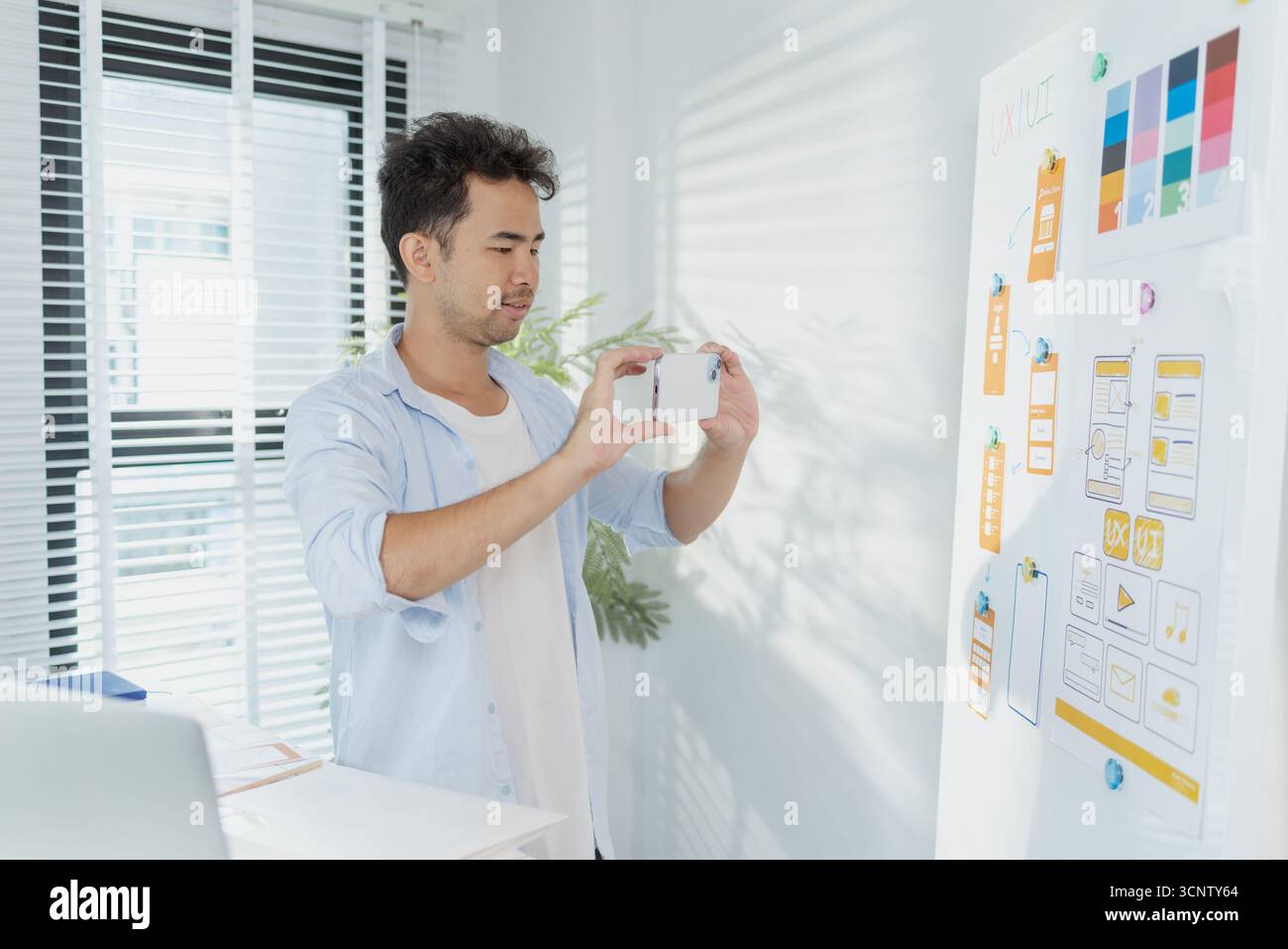 Un concepteur créatif travaille sur la planification UX/UI, analysant des croquis et des prototypes sur un tableau blanc tout en utilisant un ordinateur portable. Le processus montre la pensée de conception Banque D'Images