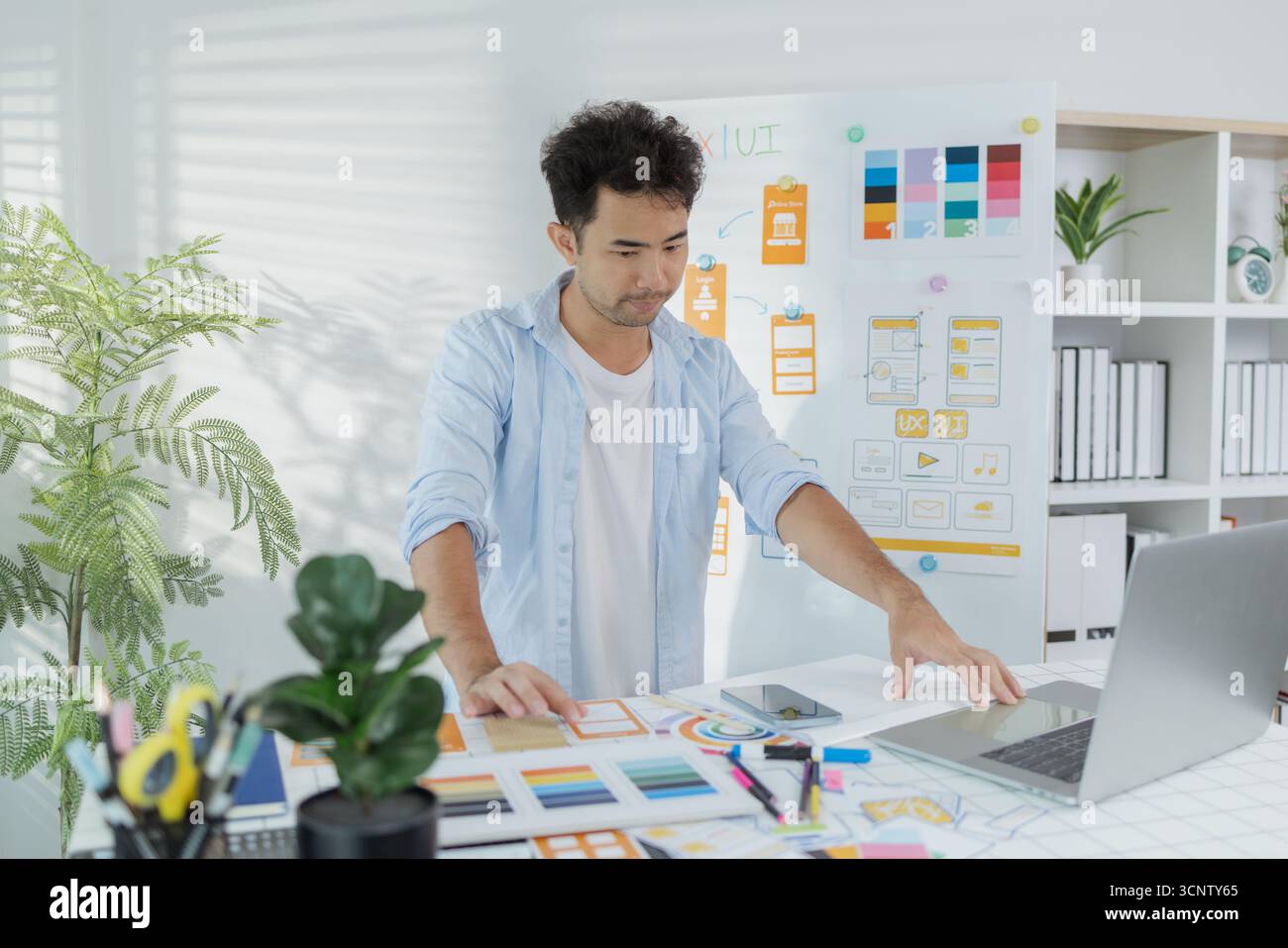 Un concepteur créatif travaille sur la planification UX/UI, analysant des croquis et des prototypes sur un tableau blanc tout en utilisant un ordinateur portable. Le processus montre la pensée de conception Banque D'Images
