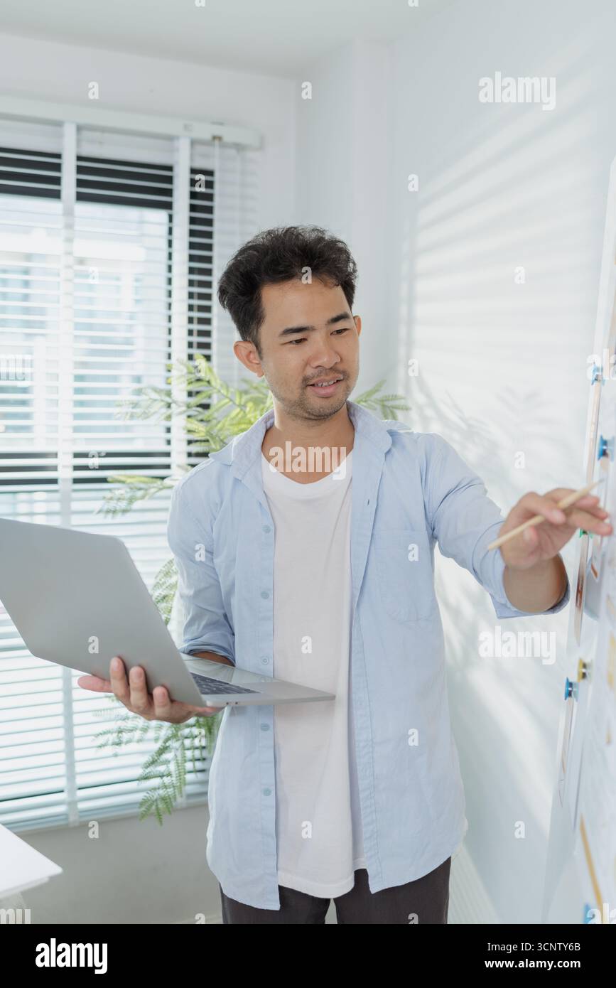 Un concepteur créatif travaille sur la planification UX/UI, analysant des croquis et des prototypes sur un tableau blanc tout en utilisant un ordinateur portable. Le processus montre la pensée de conception Banque D'Images