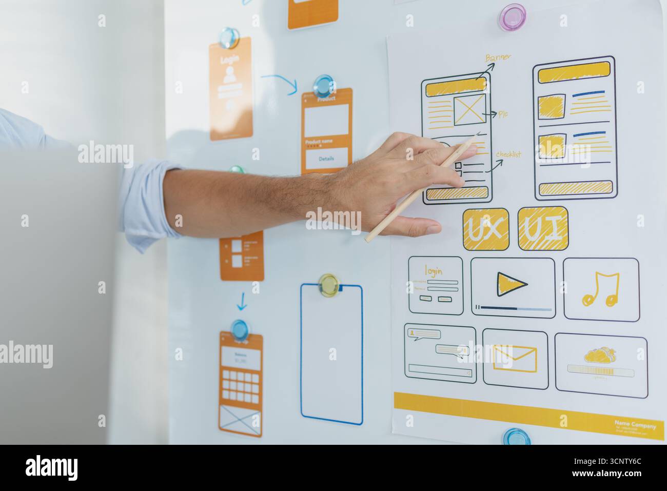 Un concepteur créatif travaille sur la planification UX/UI, analysant des croquis et des prototypes sur un tableau blanc tout en utilisant un ordinateur portable. Le processus montre la pensée de conception Banque D'Images