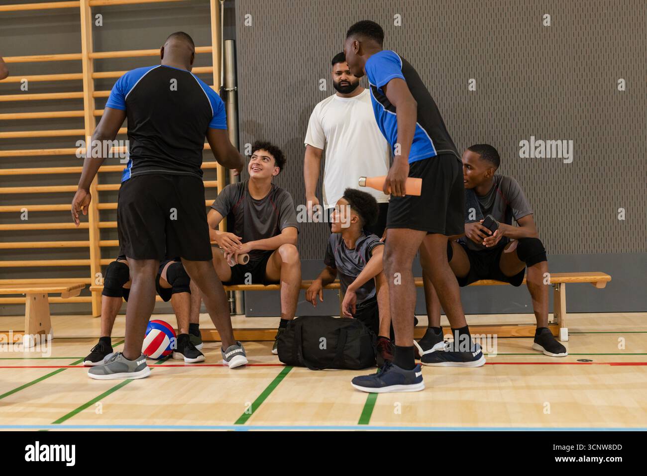 Divers coéquipiers masculins de volley-ball avec entraîneur se rassemblant sur le banc dans la salle de gym autour de l'équipement de volley-ball Banque D'Images