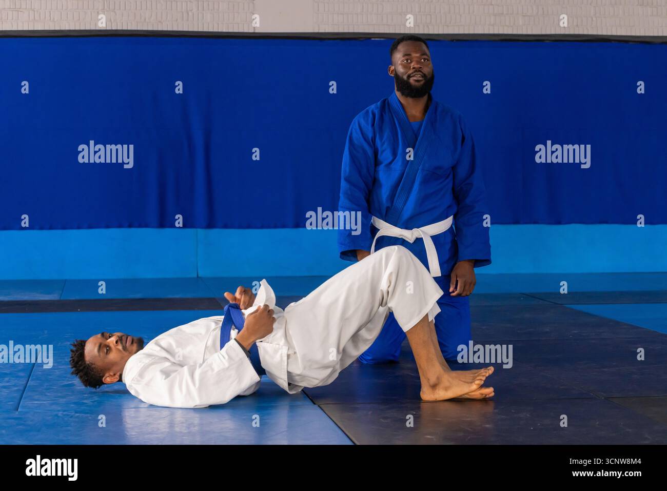 Partenaires d'entraînement masculin afro-américain pratiquant le pont de hanche dans le gymnase en sig, ceintures sur tapis Banque D'Images