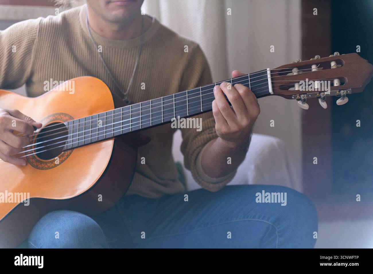 Un homme tape une guitare acoustique dans le confort de sa maison, portant une tenue décontractée. Un éclairage doux crée une atmosphère détendue et accueillante, parfaite fo Banque D'Images