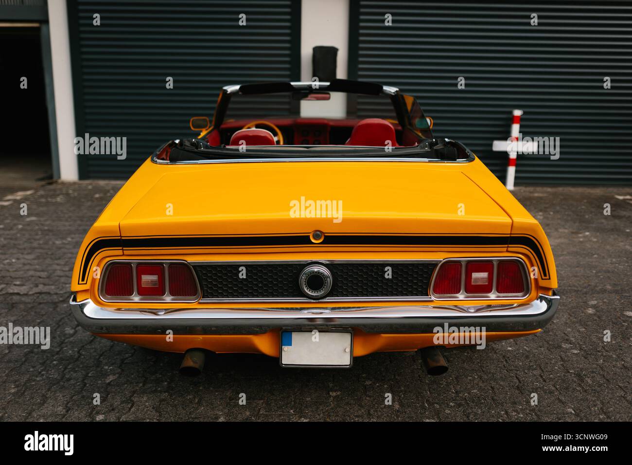 Une voiture cabriolet jaune classique est élégamment garée devant un garage aux portes blanches. La couleur vibrante met en valeur son style vintage et les horaires Banque D'Images