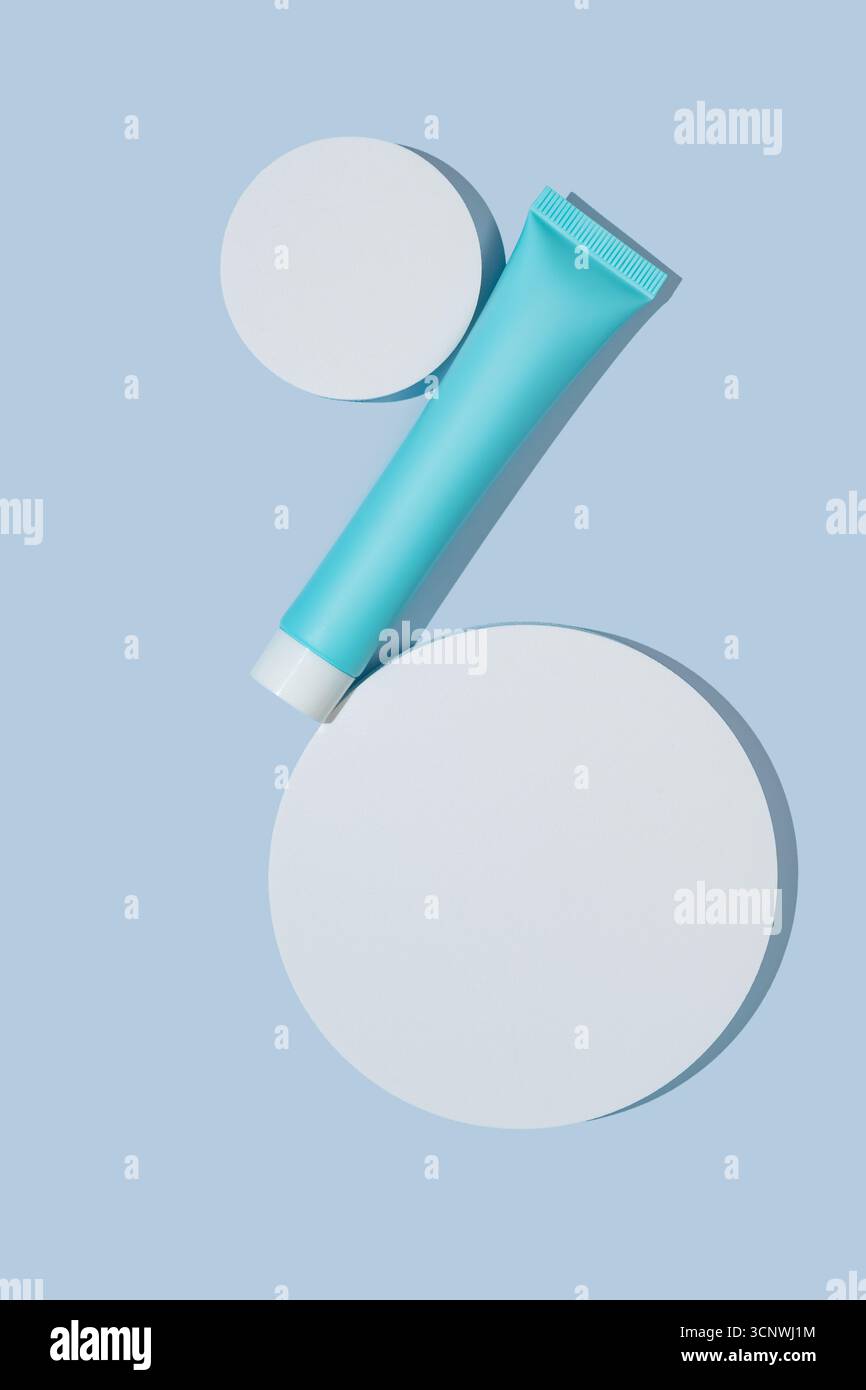 Un design minimaliste de paquet cosmétique avec un tube élégant et des formes circulaires sur un fond bleu apaisant. La composition met en valeur l'élégance et Banque D'Images