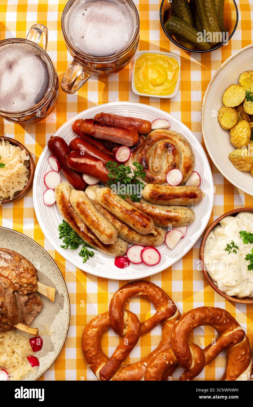 Un plat traditionnel de l'Oktoberfest composé de saucisses, bretzels, choucroute et salade de pommes de terre sur une nappe à carreaux, accompagnés de tasses Banque D'Images