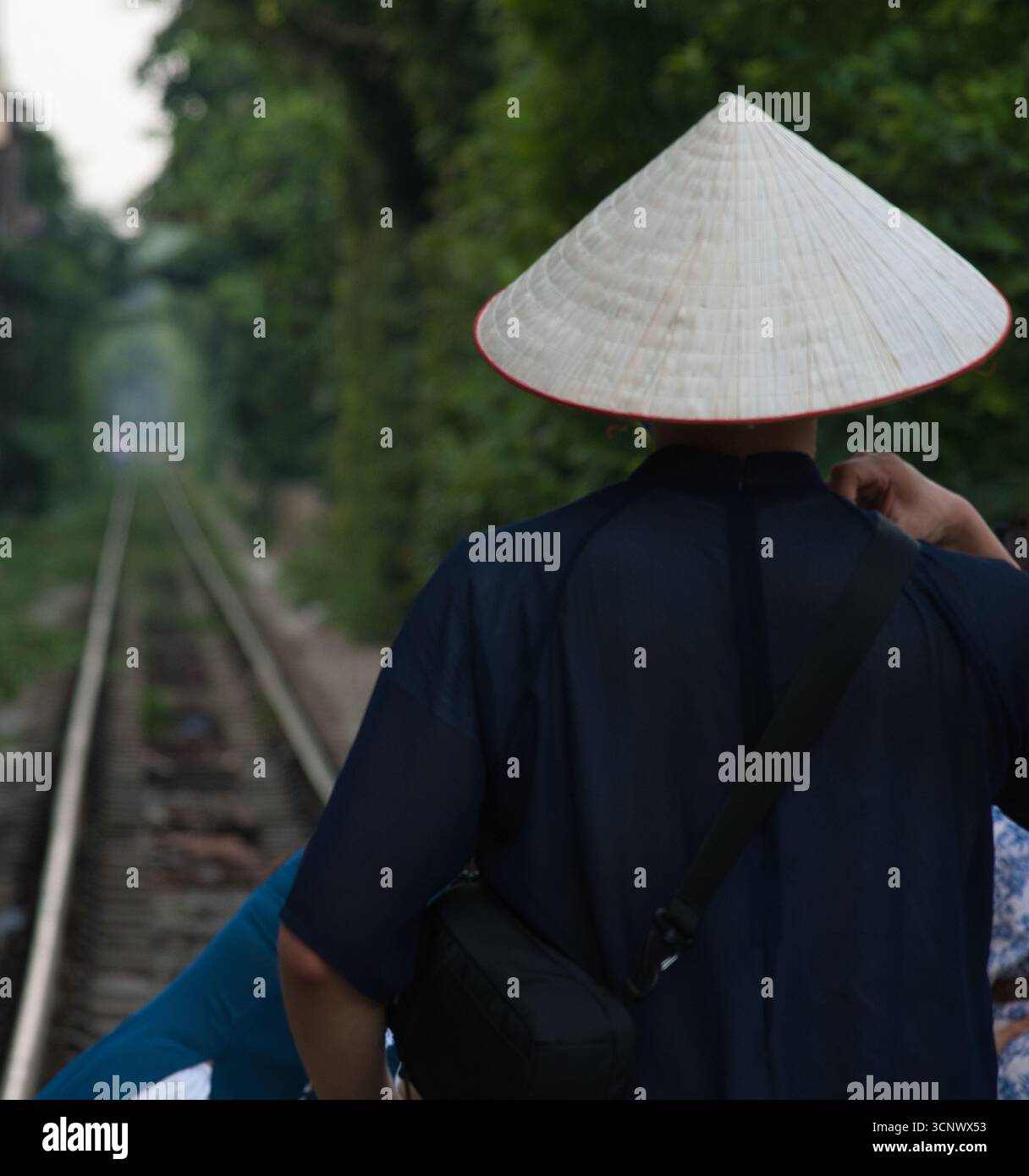 Dos de la personne portant un chapeau conique - Une personne portant un chapeau conique traditionnel, vu de derrière, debout à côté d'une voie ferrée disparaissant dedans Banque D'Images