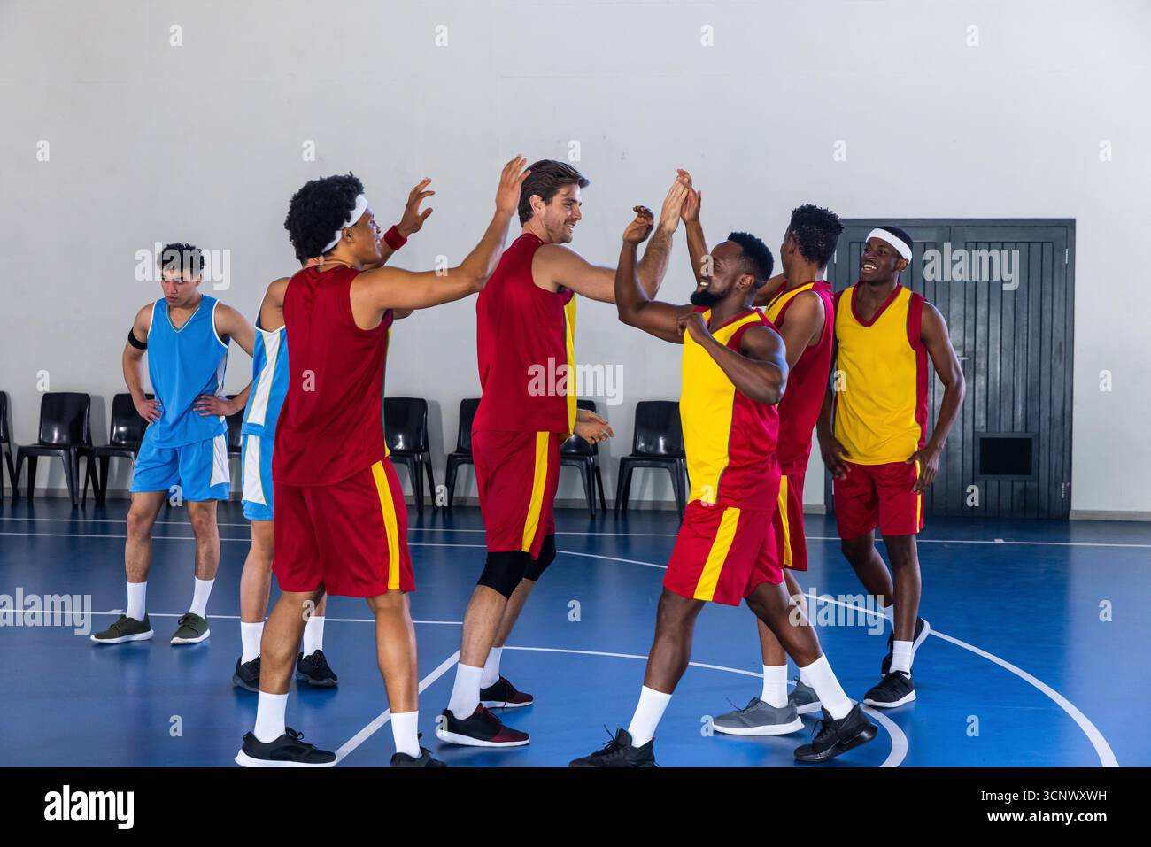 Divers joueurs de basket-ball masculins portant des uniformes rouge-jaune s'affrontent sur le terrain près des chaises Banque D'Images