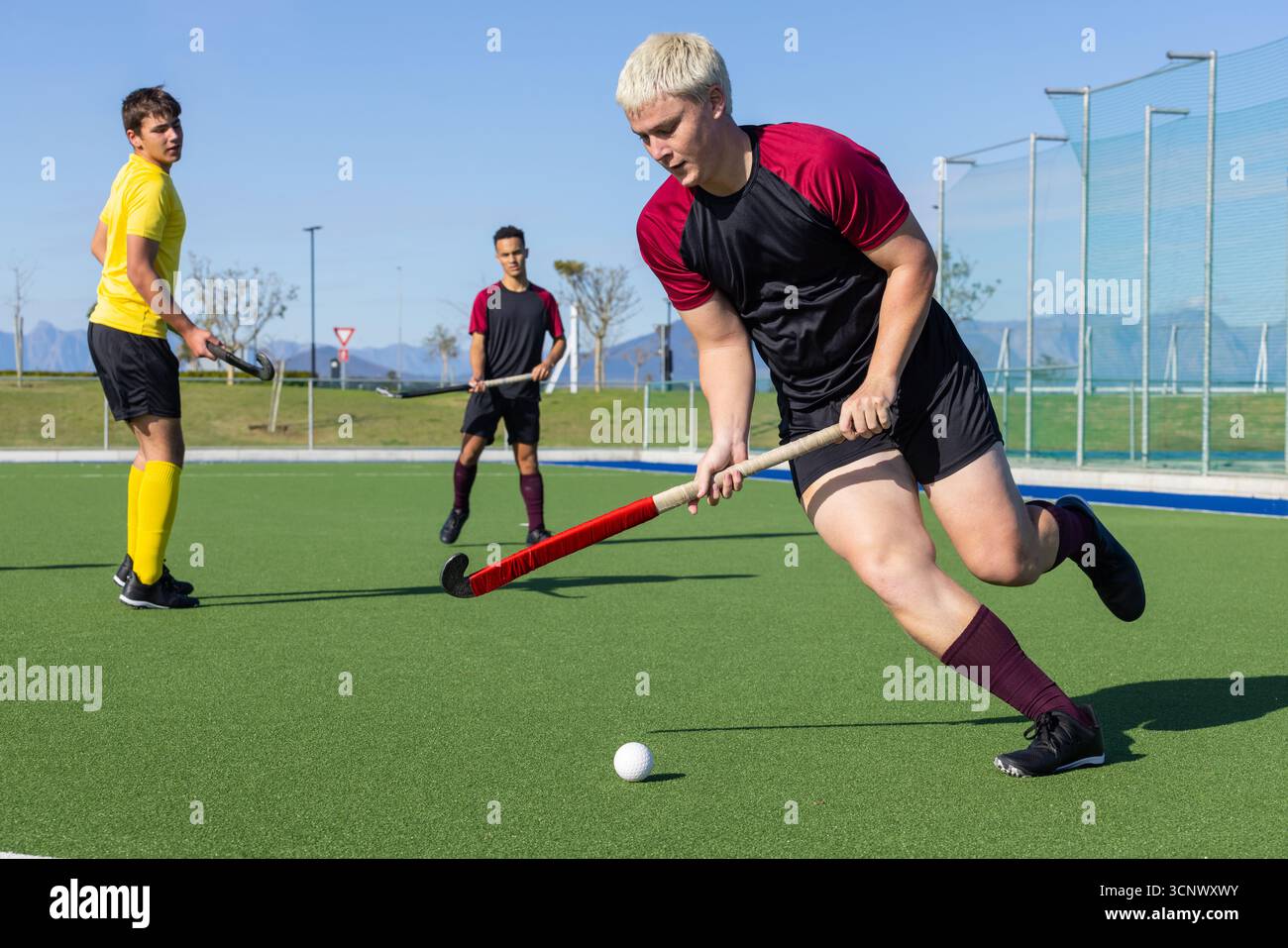 Athlète masculin blanc sprint et contrôle balle avec bâton de hockey sur gazon synthétique Banque D'Images