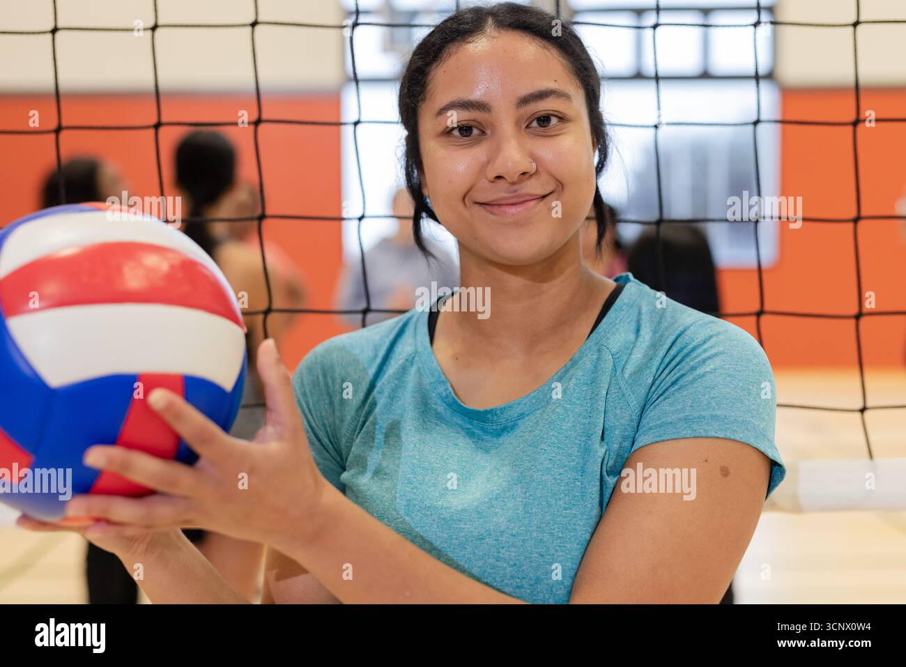 Athlète féminine portant un maillot de sport sarcelle tenant un ballon de volley rouge blanc et bleu au gymnase Banque D'Images