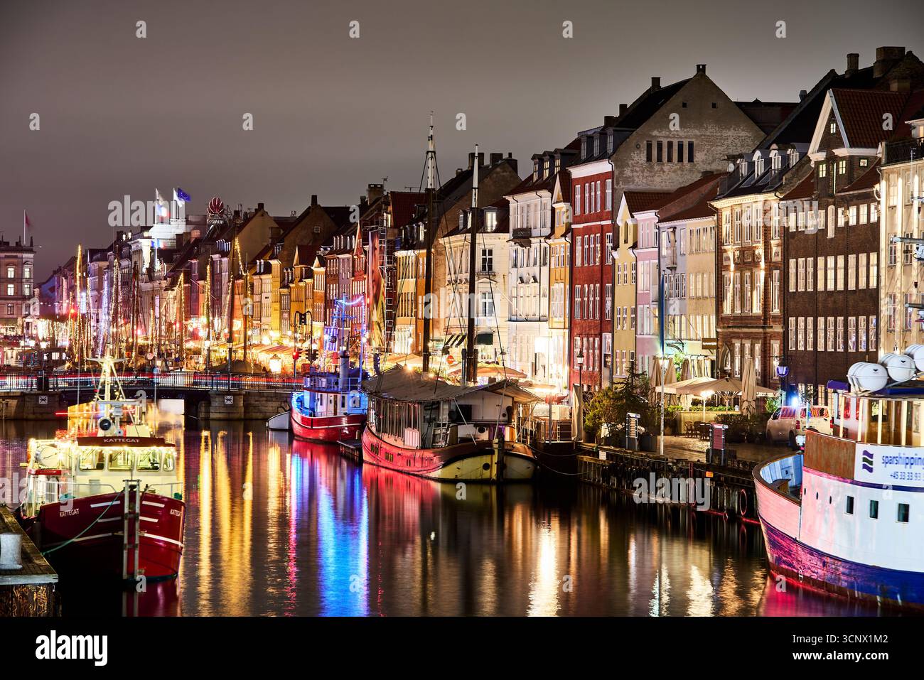 Nyhavn la nuit : des reflets vibrants scintillent sur le canal, avec des bâtiments historiques colorés et des bateaux éclairés bordant le front de mer. Copenhague, Danemark Banque D'Images