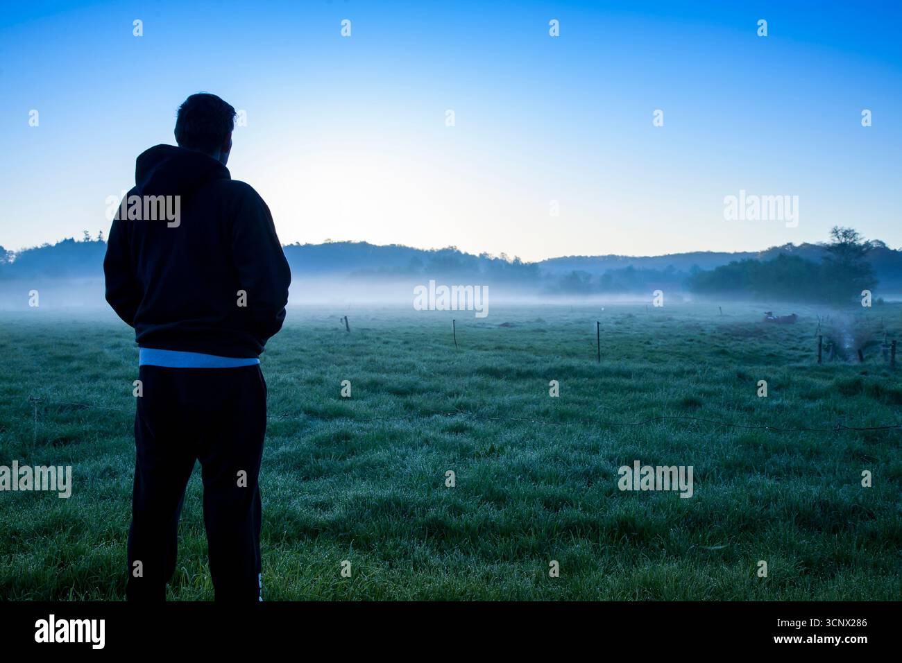 jeune homme avec dos à la caméra dans des vêtements décontractés regardant sur le paysage tôt le matin avec le brouillard et le lever du soleil, l'homme pensant dans la nature Banque D'Images