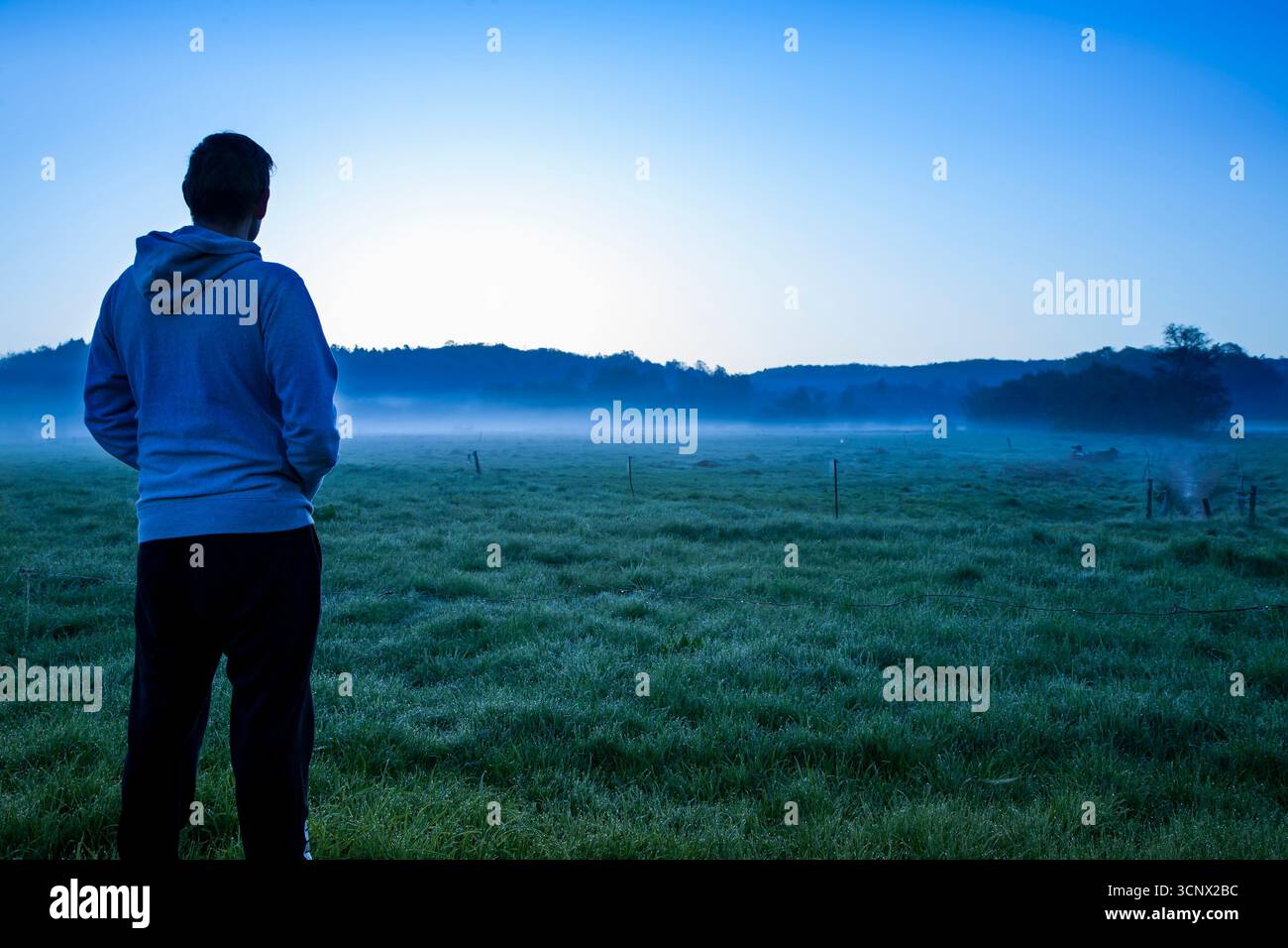jeune homme avec dos à la caméra dans des vêtements décontractés regardant sur le paysage tôt le matin avec le brouillard et le lever du soleil, l'homme pensant dans la nature Banque D'Images