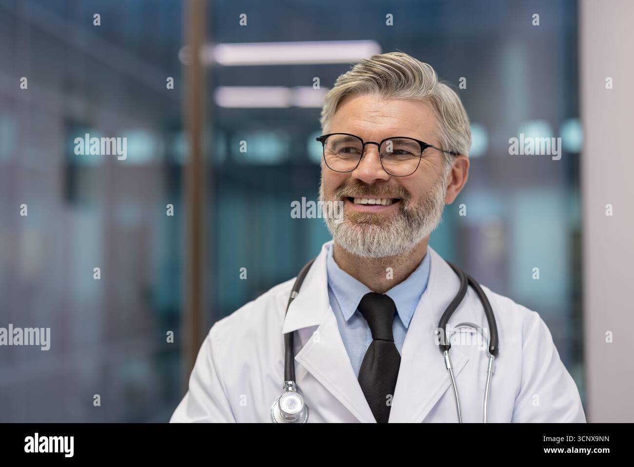 Médecin mûr souriant portant une blouse de laboratoire blanche et un stéthoscope, regardant en toute confiance dans un environnement de soins de santé moderne, représentant la sagesse et les soins professionnels Banque D'Images