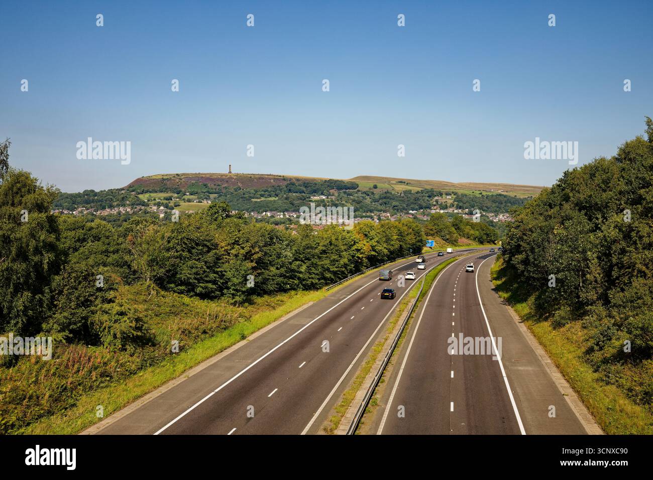 La M66 court entre les arbres avec Holcombe Moor et le Peel Monument en arrière-plan, Bury, Greater Manchester. Banque D'Images
