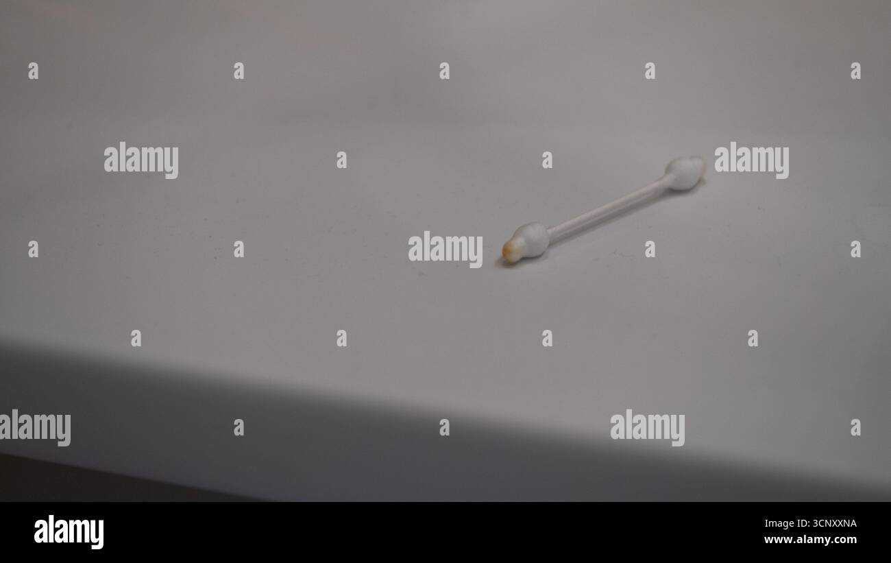 Gros plan d'un coton-tige usagé avec du cérumen sur une surface blanche de salle de bain. Image conceptuelle pour l'hygiène, les soins des oreilles, le nettoyage, les habitudes de santé et les soins médicaux Banque D'Images