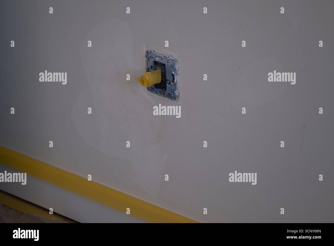 Gros plan du trou de prise électrique recouvert de ruban adhésif jaune dans le mur blanc pendant le processus de réparation et de rénovation. Idéal pour le bricolage, la construction, la sécurité, i Banque D'Images
