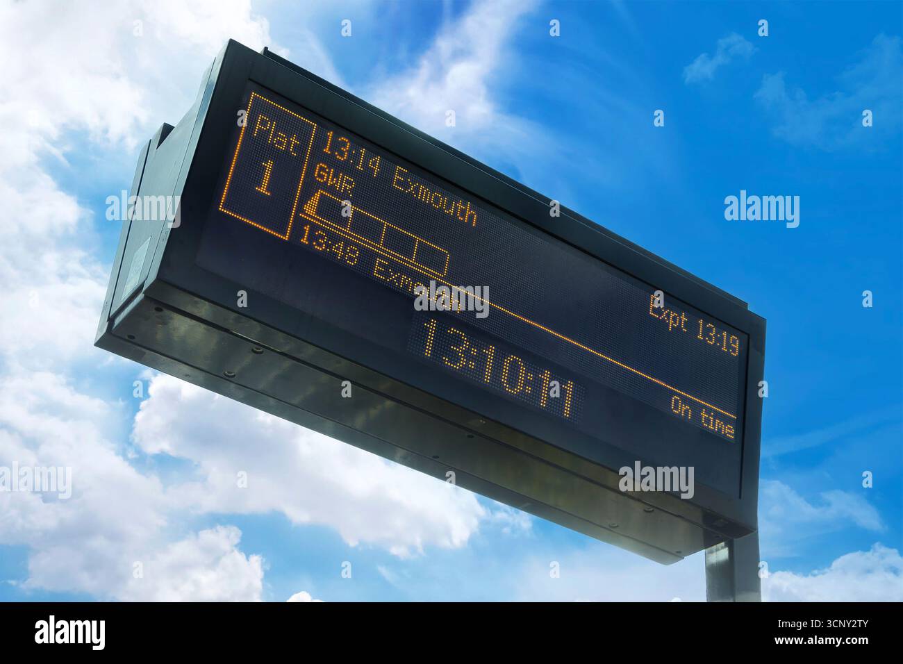 Panneau de départ de la gare numérique montrant les horaires des trains à destination d'Exmouth sur fond d'un ciel bleu et de nuages blancs UK Banque D'Images