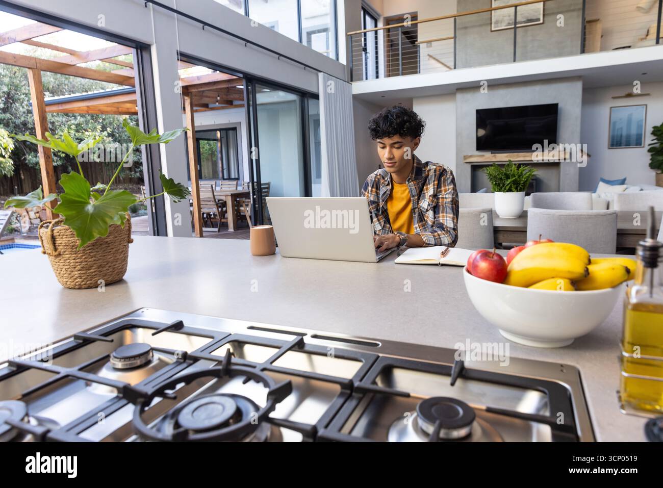 Homme travaillant sur ordinateur portable et jetant un coup d'œil à ordinateur portable à la cuisine par table de cuisson à gaz, espace de copie Banque D'Images