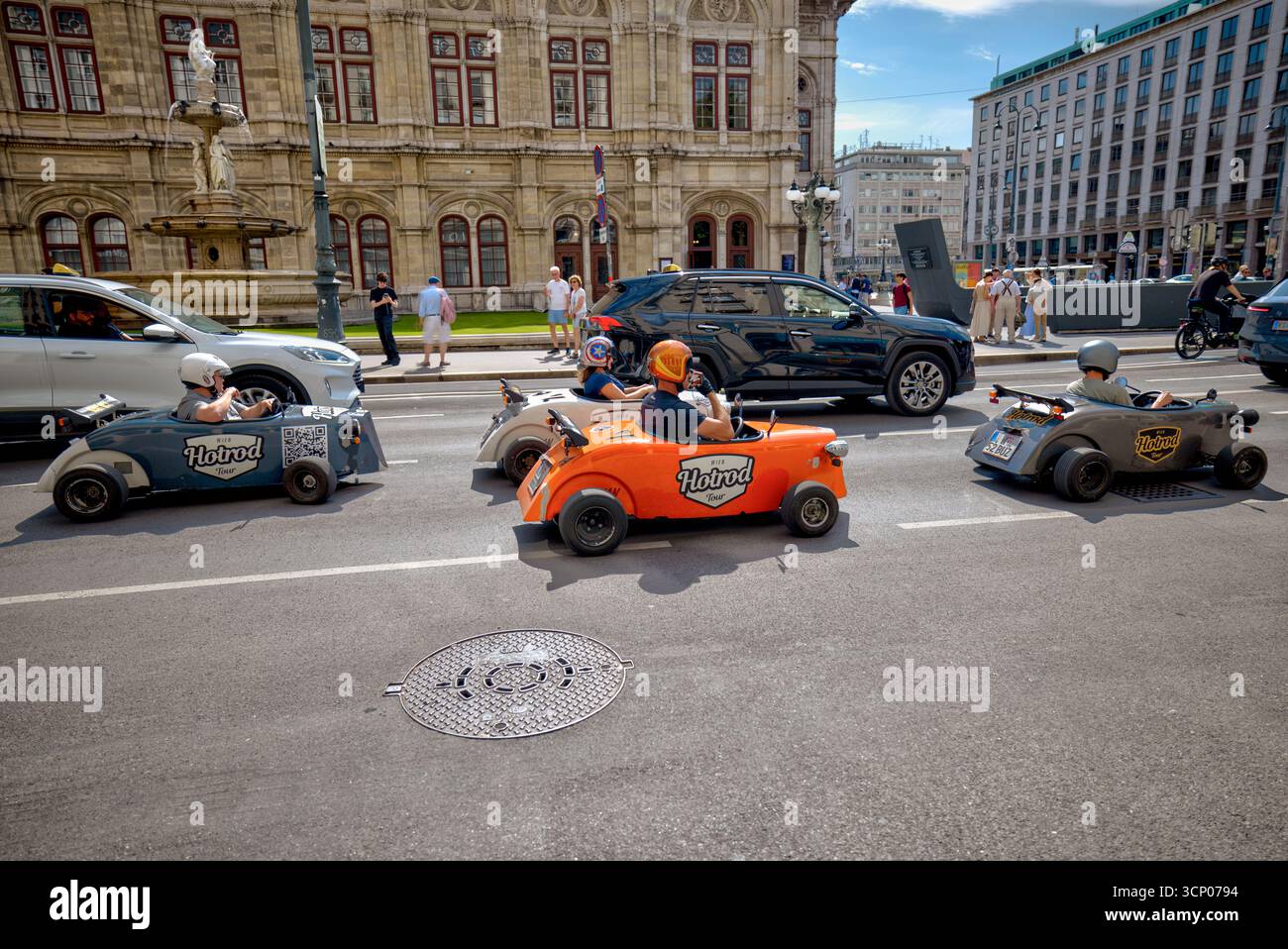 Les touristes passent devant l'Opéra national de Vienne dans des mini hot rods aux couleurs vives lors d'une visite guidée de la ville. Banque D'Images