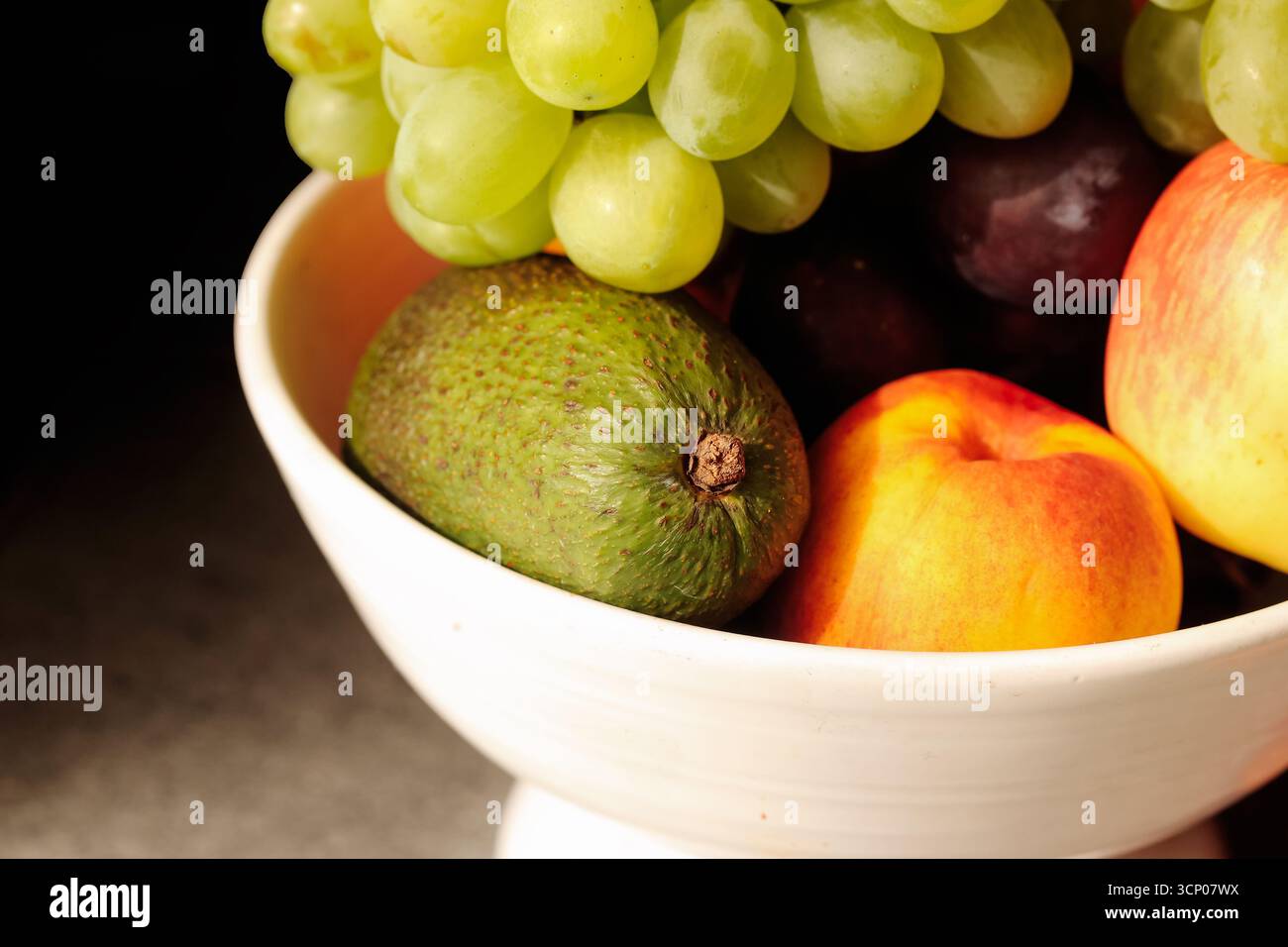 Fruits frais mélangés dans un bol. Avocat avec raisins et pêche. Pomme avec prune et agrumes. Récolte saisonnière naturelle du verger. Banque D'Images
