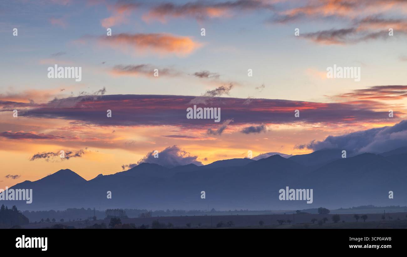 Silhouettes de montagne sous un ciel peint, les teintes douces du lever du soleil enflamment l'horizon. Le spectacle de la nature se déroule. Banque D'Images