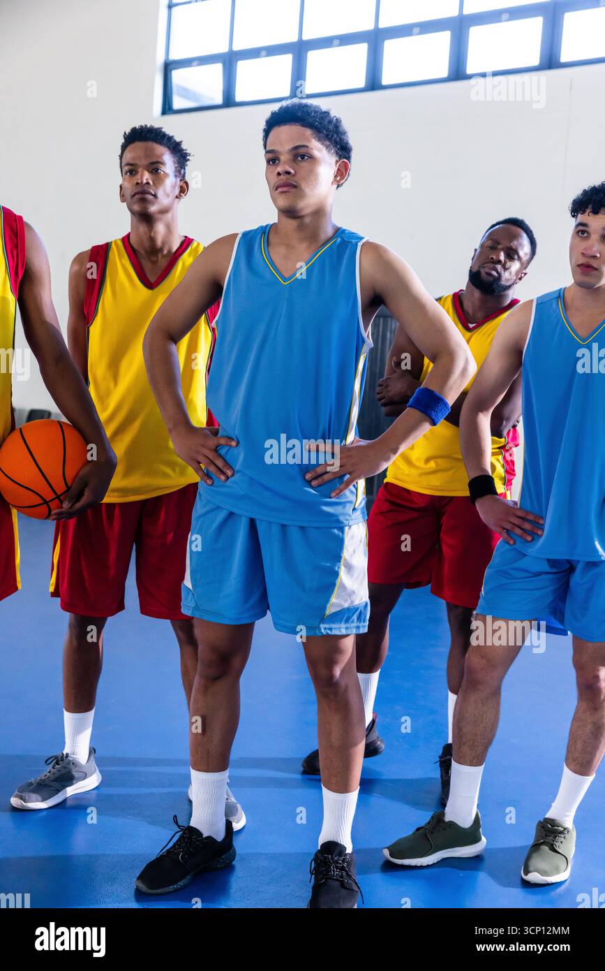 Joueurs de basket-ball afro-américains debout sur le terrain bleu tenant le ballon sous de hautes fenêtres Banque D'Images