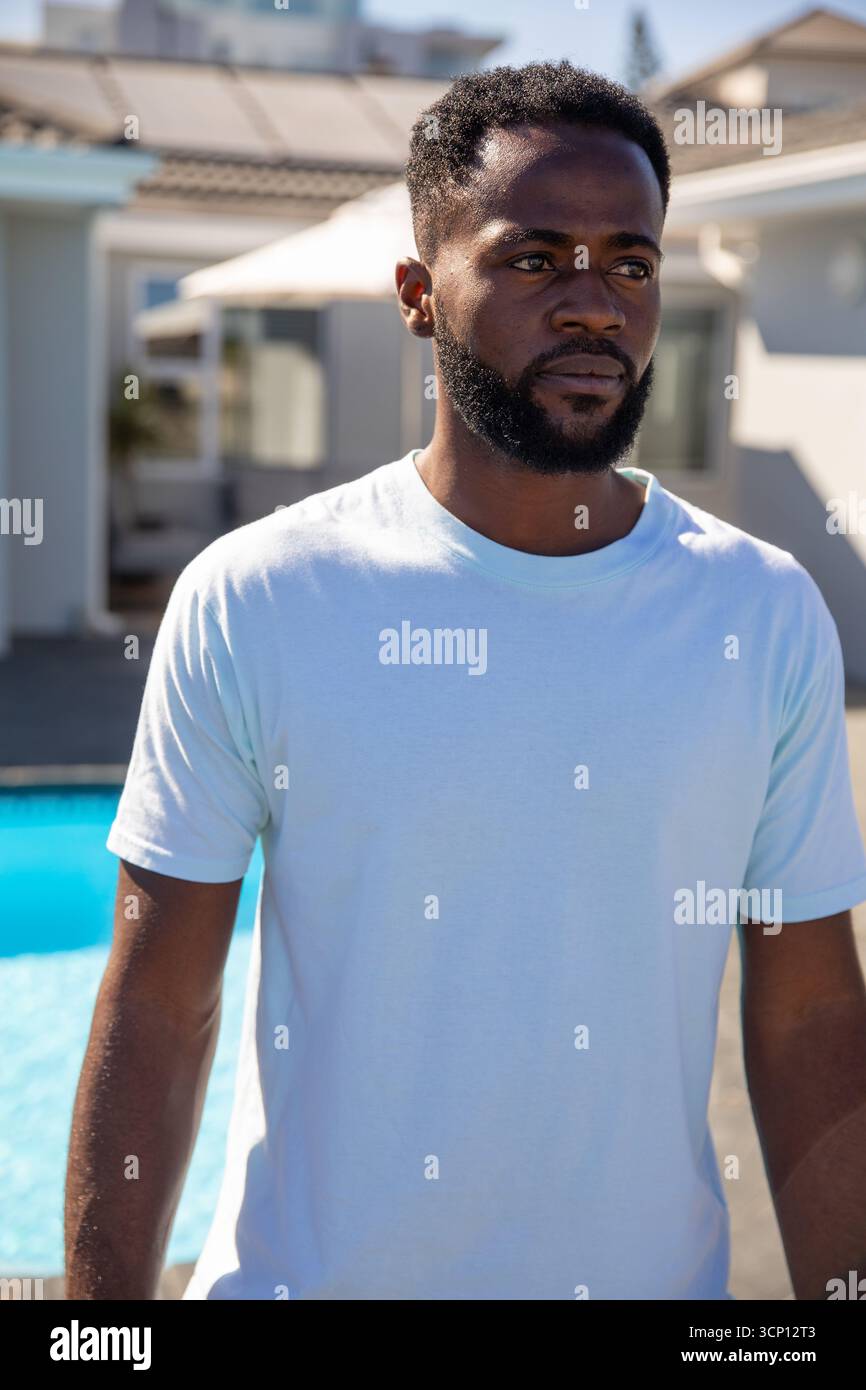 Homme afro-américain près du bord de la piscine dans la cour arrière par parasol de patio Banque D'Images