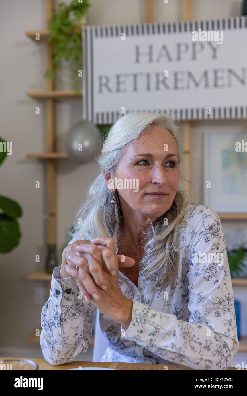 Femme âgée assise à table dans une pièce décorée sous signe de retraite heureuse avec ballon Banque D'Images