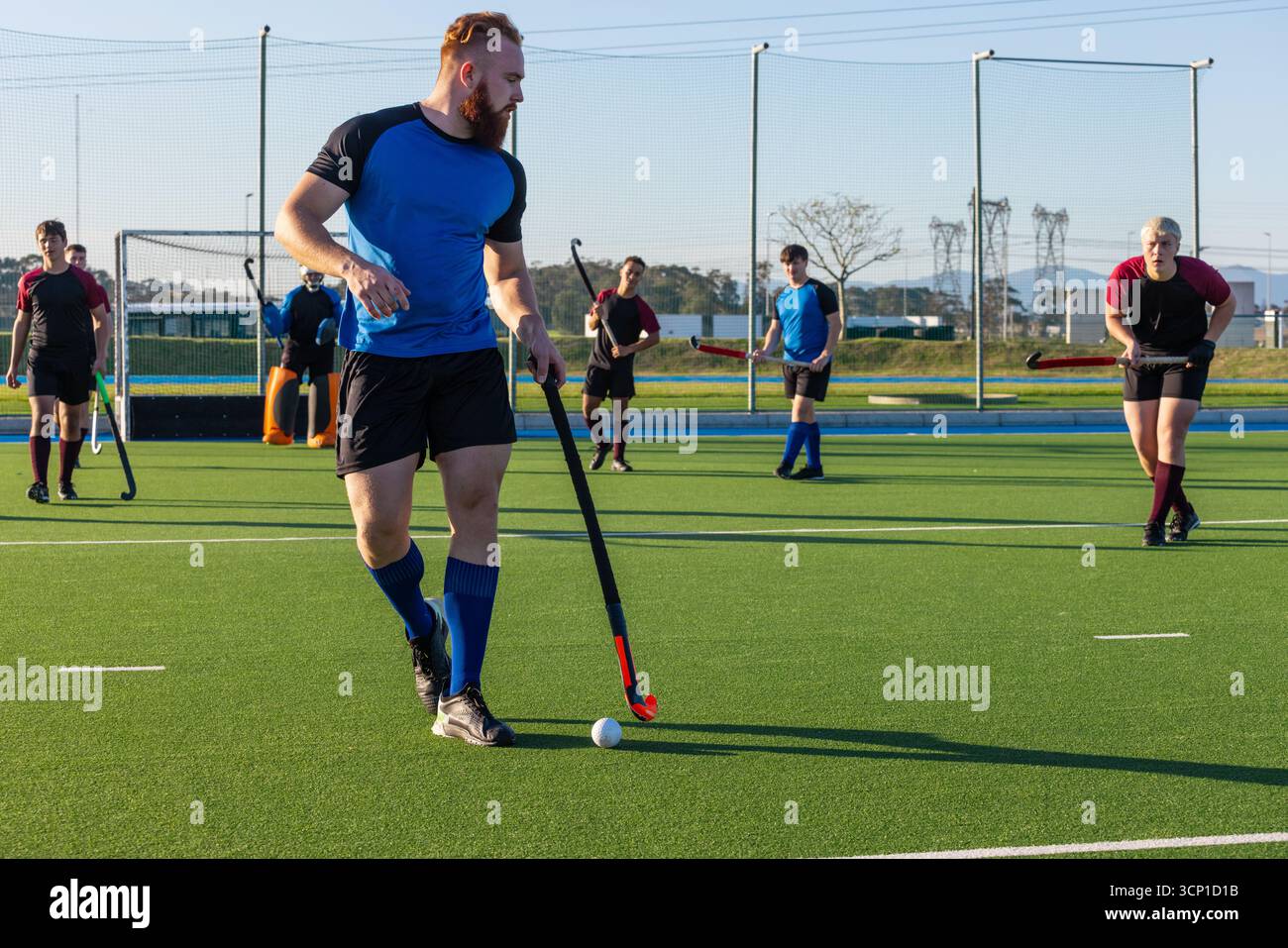 Joueur masculin de hockey sur gazon en maillot bleu et noir dribble balle blanche avec bâton sur gazon Banque D'Images