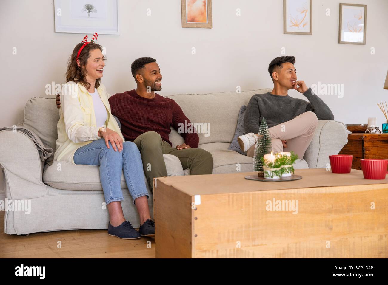 Divers amis assis sur le canapé gris dans le salon portant la canne à bonbons et bois tenant des tasses rouges Banque D'Images