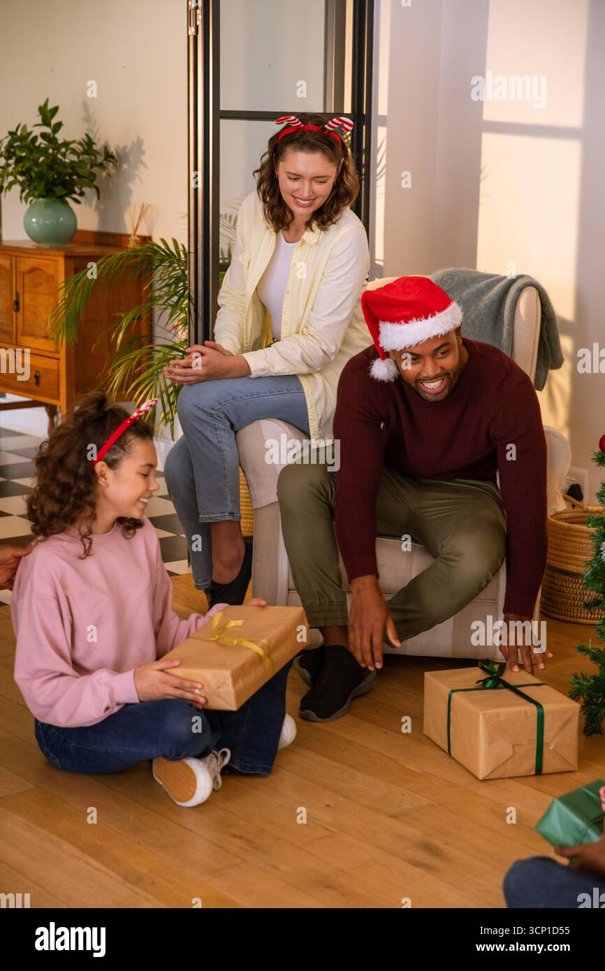 Famille diversifiée portant des chapeaux de père noël rassemblant autour de cadeaux enveloppés dans le salon Banque D'Images