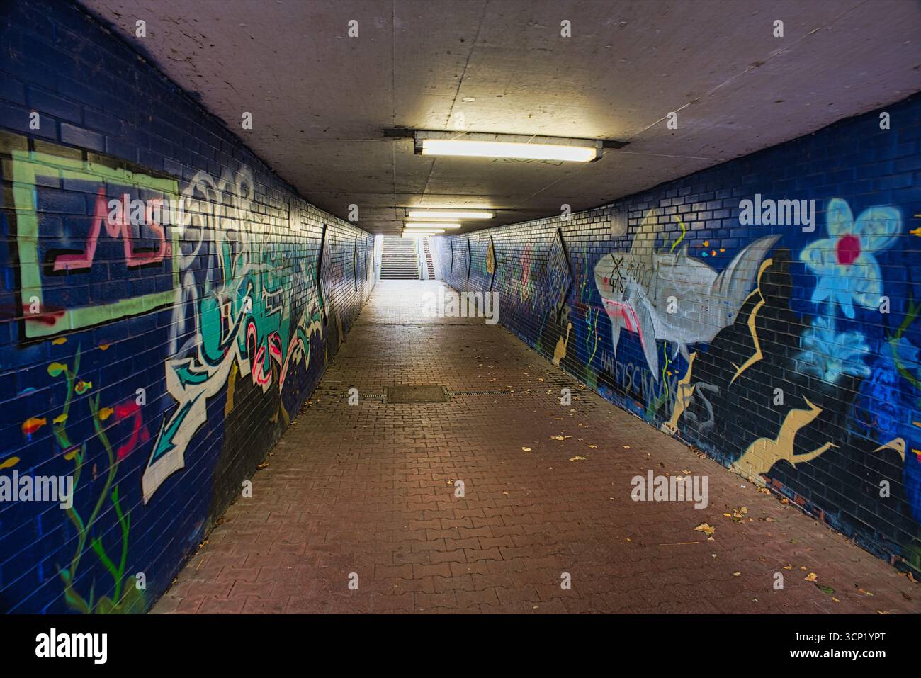 Tunnel urbain souterrain avec des peintures murales graffiti colorées et du Street Art sur des murs de briques bleues Banque D'Images