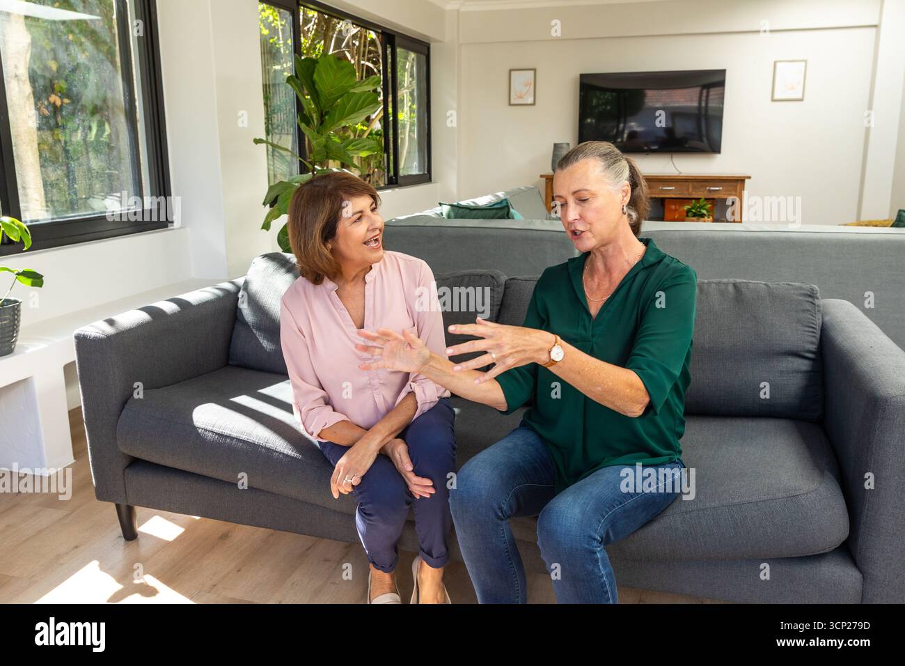 Diverses amies féminines, une aînée, assise sur le canapé dans le salon, faisant des gestes près de la télévision à écran plat Banque D'Images