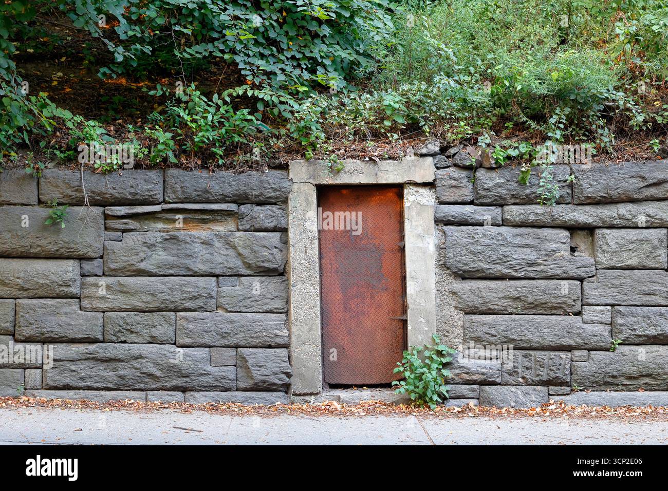 Une porte en tôle d'acier rustique abandonnée dans un mur de pierre de granit le long de la transversale de la 86e rue dans Central Park de Manhattan, New York City. Banque D'Images