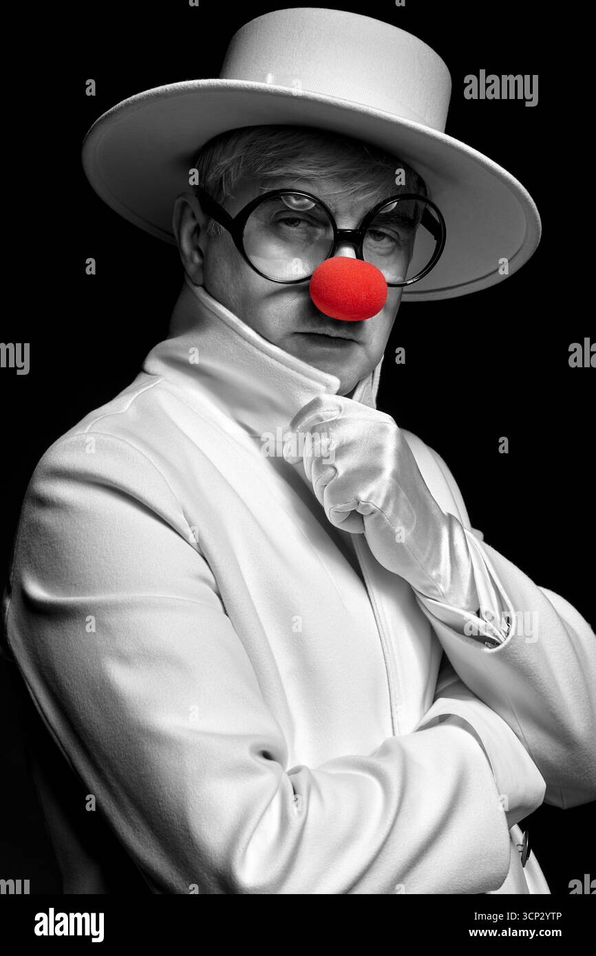 Gros plan portrait couleur sélectif du clown triste. Un homme âgé dans un manteau blanc et un chapeau sur fond noir. Banque D'Images