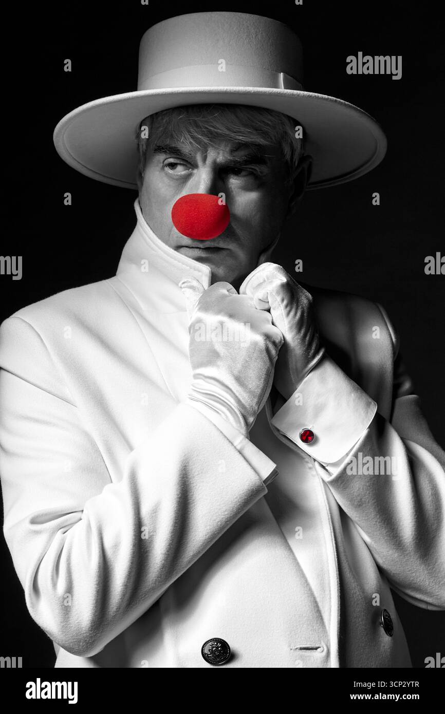 Gros plan portrait couleur sélectif du clown triste. Un homme âgé dans un manteau blanc et un chapeau sur fond noir. Banque D'Images