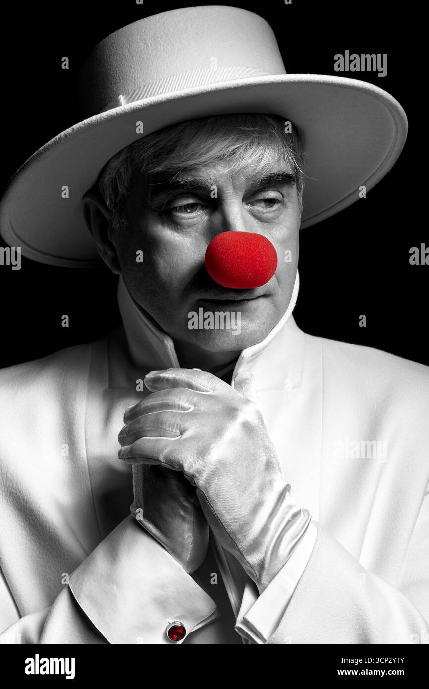 Gros plan portrait couleur sélectif du clown triste. Un homme âgé dans un manteau blanc et un chapeau sur fond noir. Banque D'Images