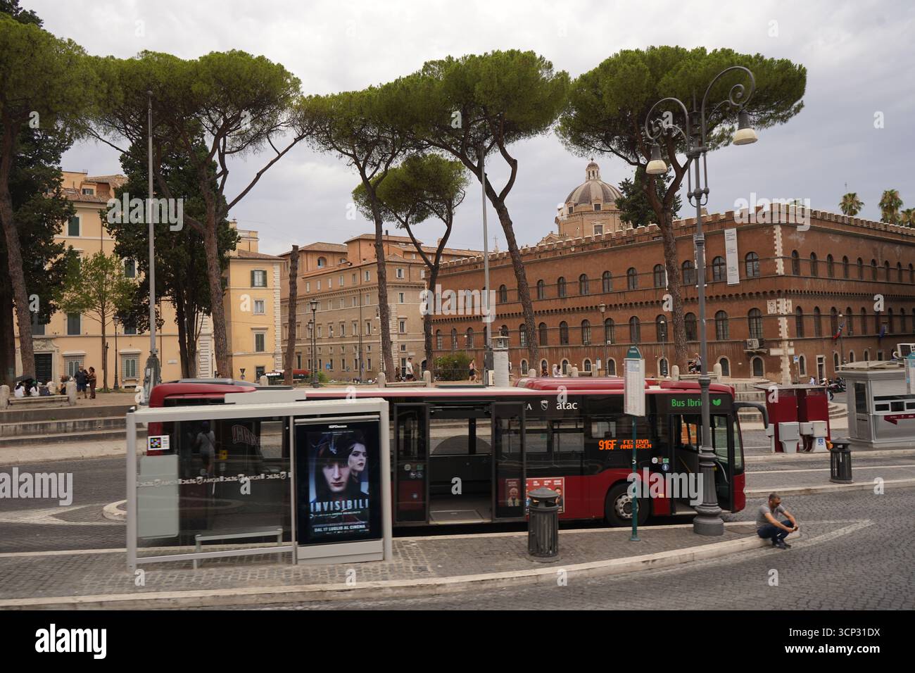 Un bus touristique à impériale à un arrêt près des bâtiments historiques. Le bus rouge est garé avec un homme assis sur le trottoir à proximité. Banque D'Images