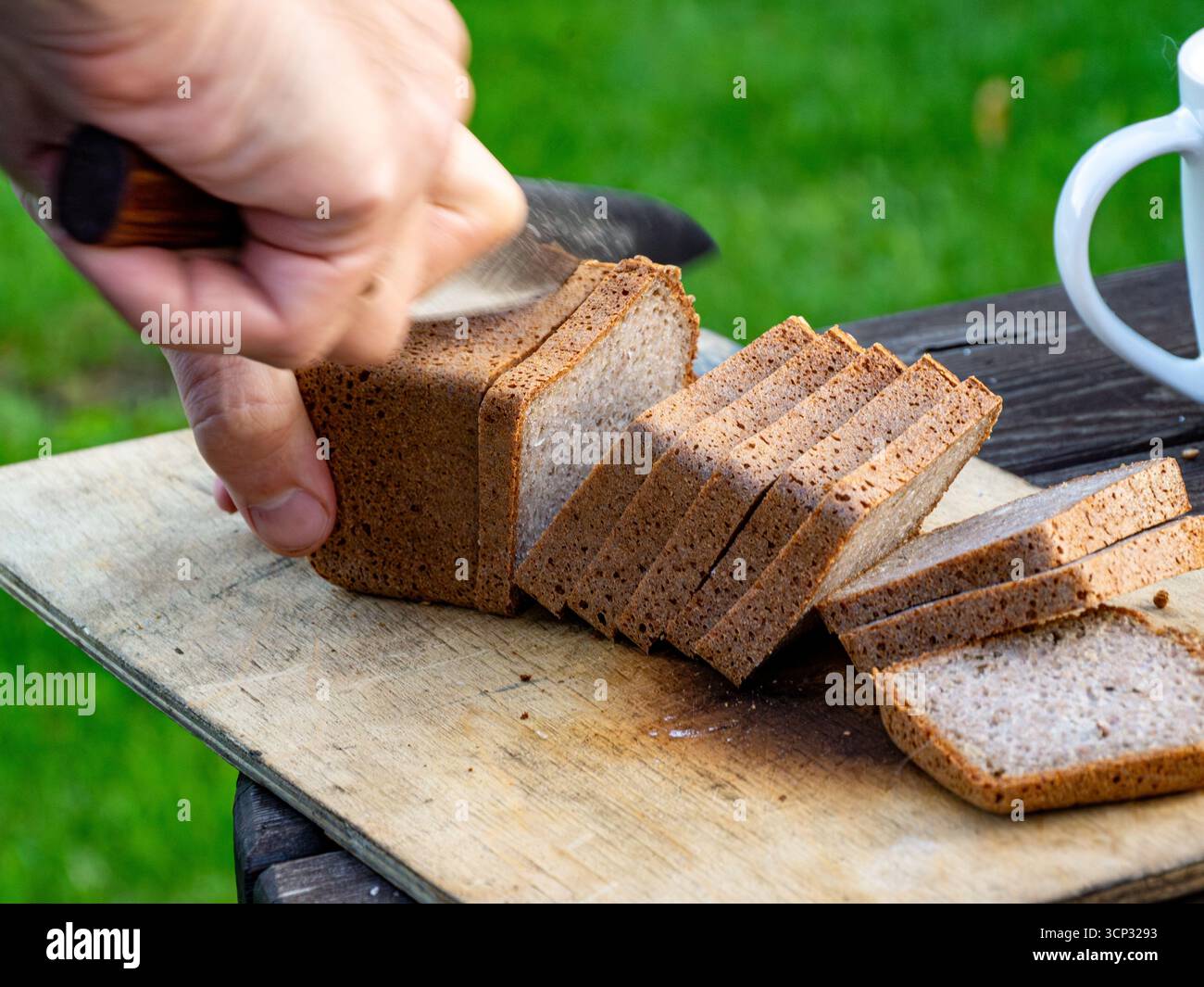 Une personne coupe des tranches épaisses de pain de seigle à grains entiers à l'aide d'un couteau tranchant révélant une structure de miettes serrée avec une mise au point sélective Banque D'Images