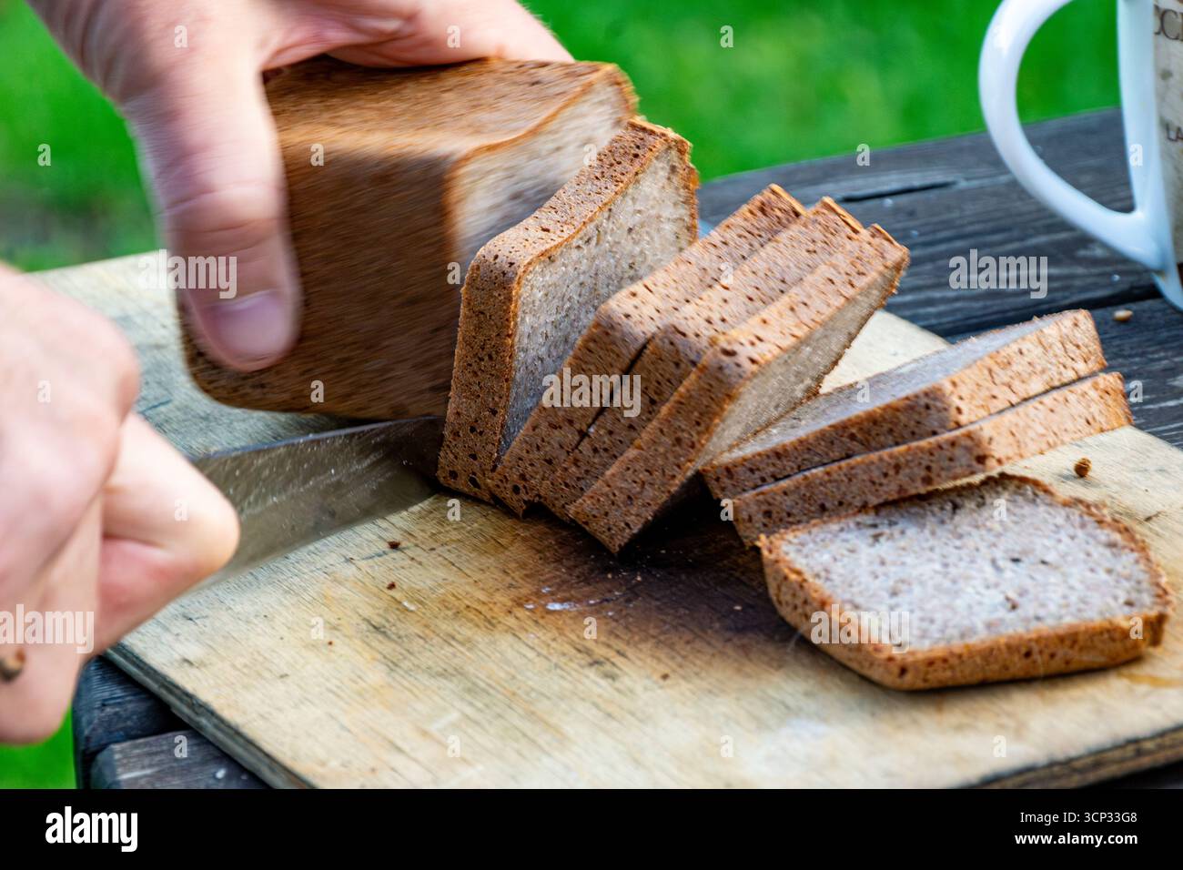 La main se déplace rapidement en tranchant le pain de seigle créant un flou de mouvement tandis que le couteau sépare la miette dense avec la profondeur de champ Banque D'Images