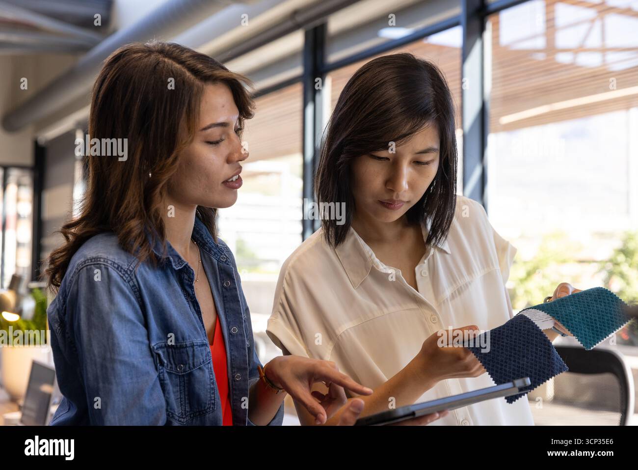 Diverses collègues féminines collaborant sur la sélection de tissus à l'aide d'une tablette au bureau Banque D'Images