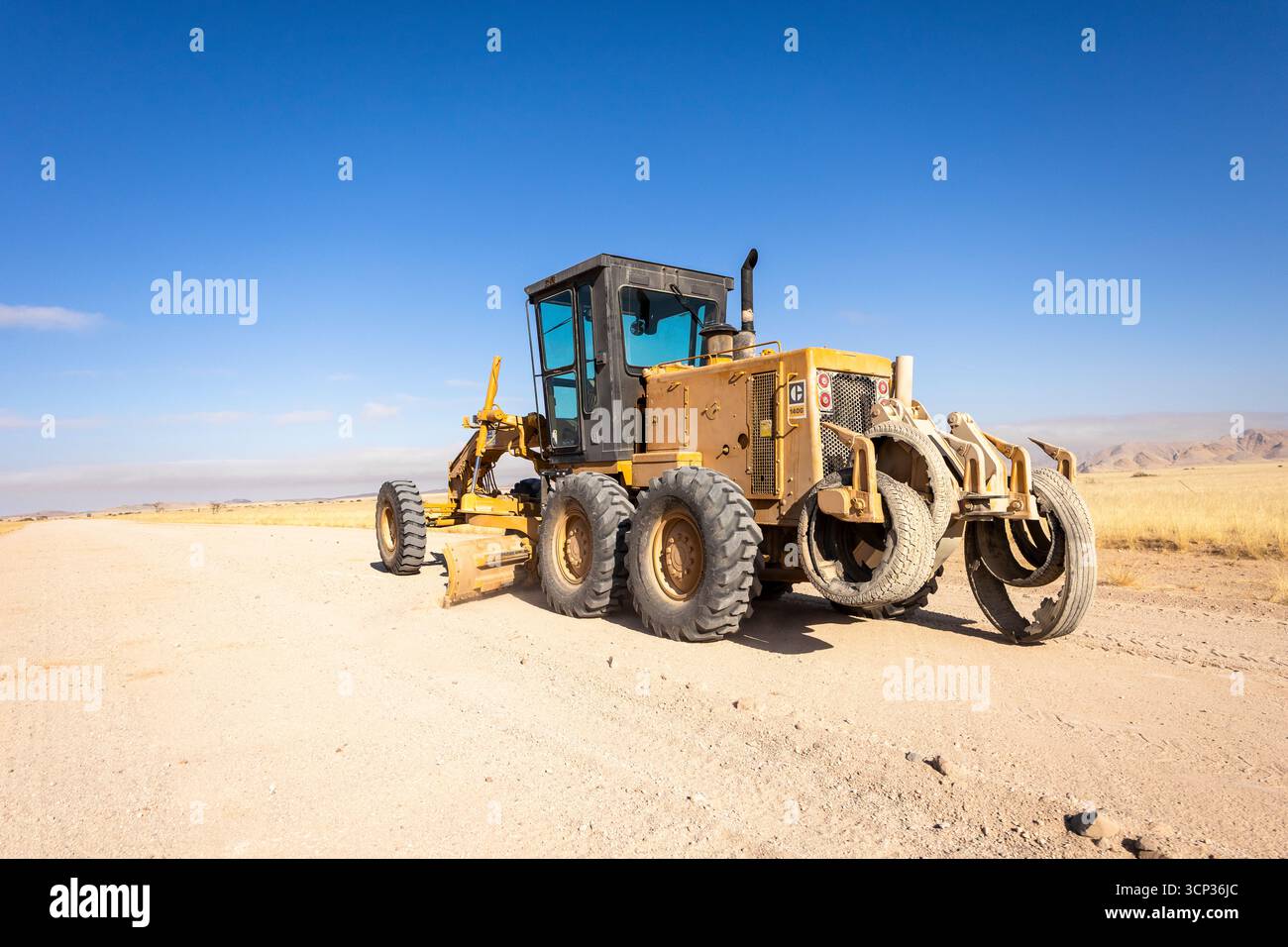 Dans le désert isolé près de Solitaire, en Namibie, un tracteur plane un chemin de terre à travers des dunes de sable doré et un terrain désertique accidenté Banque D'Images